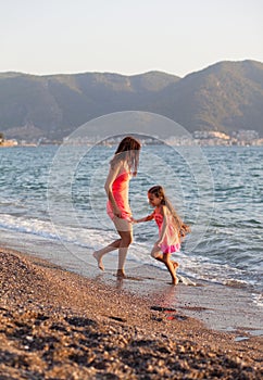 Mother and her little daughter playing and running on the beach