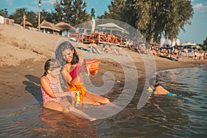 Mother and her little happy daughter are playing with beach toys in the water