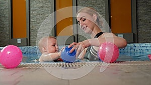A mother and her little one-year-old daughter are playing in a pool with balls.