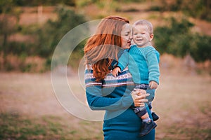 Mother and her little son in a knitwear have a walk in a forest