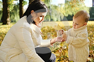 Mother with her little son walks in the autumn park. Mother gives her son an autumn yellow leaf