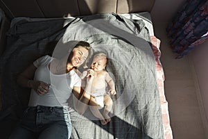 Mother with her newborn son lay on the bed in the rays of sunlight