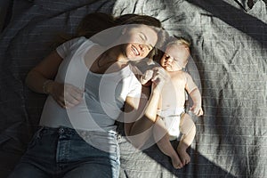 Mother with her newborn son lay on the bed in the rays of sunlight