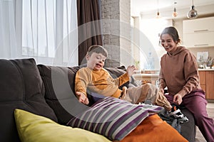 Mother and her son with Down syndrome playing at the sofa at the living room