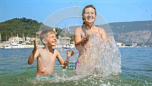Mother and her son playing and splashing water at the sea beach. Family holiday, vacation memories, and the pure joy of