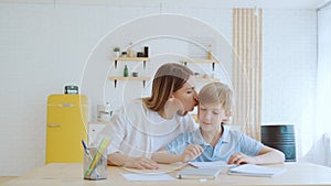 Mother and her son schoolboy do homework together at home, sitting by the table