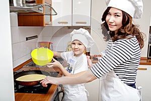 Mother and her son in white chef hats preparing an omelet in the kitchen.