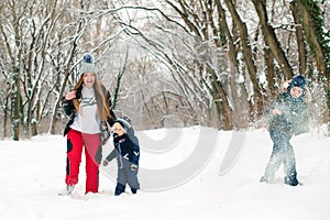 Mother and her sons plays with snow in a park. Winter time. Winter family vacation