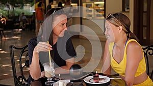 A mother and her teenage daughter are sitting in a summer cafe.
