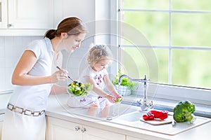 Mother and her toddler daughter washing vegetables