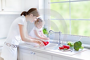 Mother and her toddler daughter washing vegetables