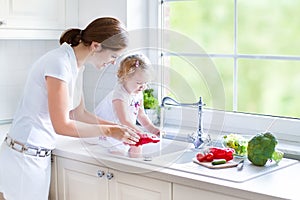 Mother and her toddler daughter washing vegetables