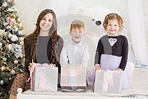 Mother and her two little children with Christmas gift boxes. Family on Christmas eve. Mother and little kids opening Xmas