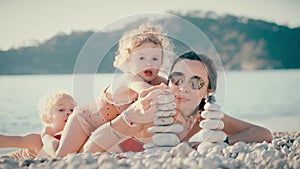 Mother and her two little girls having a good time on the beach. Building a pebble tower, faamily life balance concept