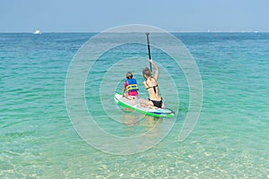 Mother and his adorable little daughter sitting on stand up board having fun during summer beach vacation