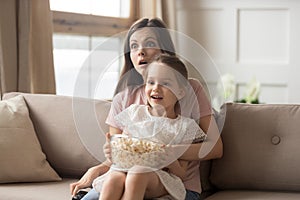 Mother hold daughter on lap watching movie feels shocked