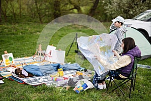Mother hold europe map, with children sit on chair against car on picnic