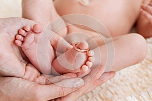 Mother hold feets with gold ring of newborn baby