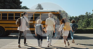 Mother hold hand schoolboy walking to bus. Energetic pupils running crossway.