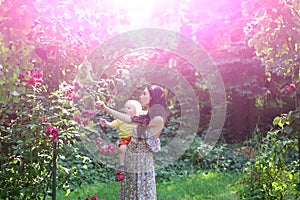 Mother hold son at blossoming roses on idyllic sunny day