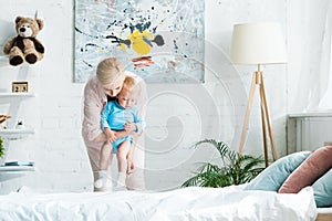 Mother holding in arms cute toddler son in bedroom