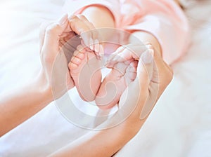Mother holding baby feet. Closeup of tiny newborn baby feet held by a parent. Small baby toes. Little baby lying on a