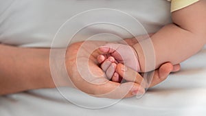 Mother holding baby hand and showing finger and fingernail on white sheet bed