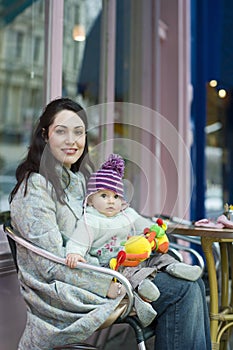 Mother Holding Baby On Lap Sitting In Outdoor Cafe