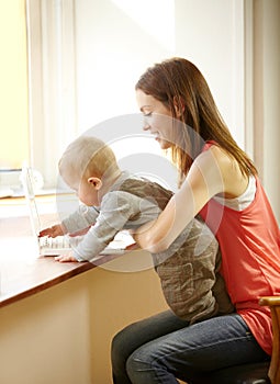 Mother, holding and baby with laptop in home for remote, work or bond with child in kitchen. Young woman, parenting and