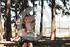 Mother holding baby little girl in her arms while standing on a bench in the park