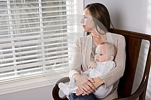 Mother holding baby in rocking chair by window