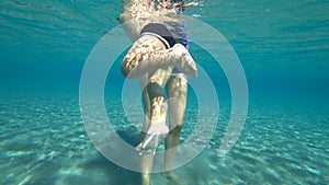 Mother holding baby in the water, boy tries to swim in the sea. Boy actively moves his legs in the water