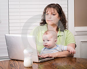 Mother holding baby while working on computer