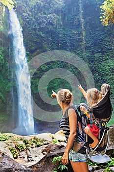 Mother holding child in backpack explore rainforest waterfall