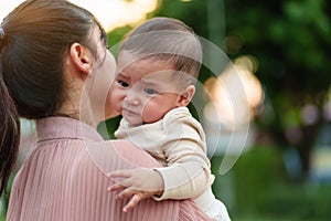 mother holding and comforting her crying infant baby outside in park with sunlight