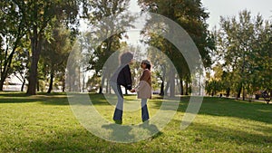 Mother holding daughter hands gently touching noses on sunny green park field.