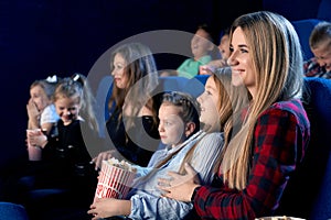 Mother holding daughter on knees in cinema.
