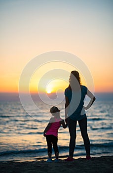 Mother holding daughters hand at sunset looking out to sea