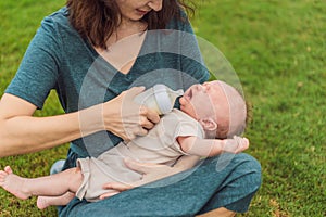 Mother holding and feeding baby from milk bottle in the park. Portrait of cute newborn baby being fed by her mother