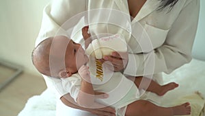 Mother holding and feeding a newborn baby boy from bottle at home