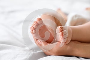 Mother holding feet of her little baby on bed. Space for text