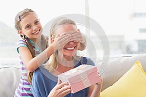 Mother holding gift with daughter covering her eyes