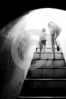 Mother holding hand her son walking up the stairs to bright sun light at the end of dark tunnel