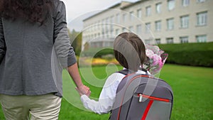 Mother holding hand of little son with backpack going to school outdoors, First-grade student, primary school, first