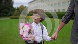 Mother holding hand of little son with backpack going to school outdoors, First-grade student, primary school, first