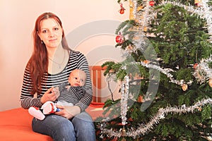 Mother holding hand of newborn baby boy by Christmas tree