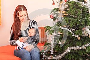 Mother holding hand of newborn baby boy by Christmas tree