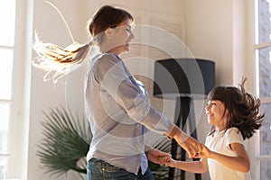 Mother holding hands with daughter dancing and jumping at home