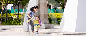 A mother is holding hands to help her son learn to walk first step, Family enjoying a stroll in the park on a sunny summer day.