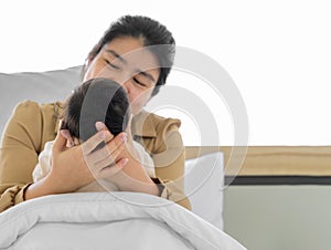 Mother holding head of her newborn baby girl or boy in hands. Loving mum sitting in white bed and holding infant child